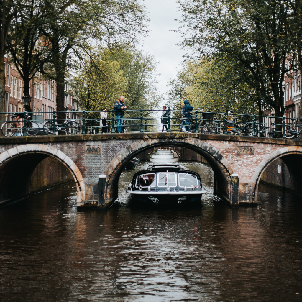 A three arched low bridge over a canal in the Netherlands with a boat sailing through the middle span while people walk or cycle across the bridge